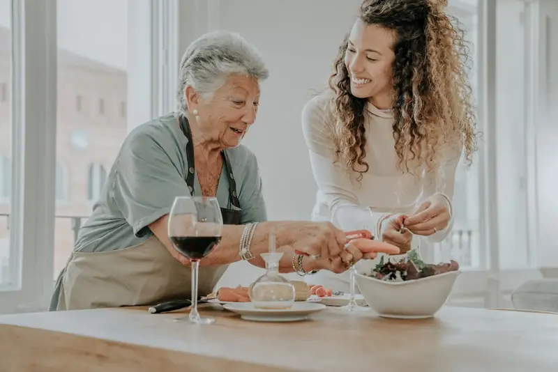 A Care Professional and an older woman preparing a meal together at home